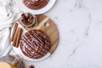 Photo of Tasty cinnamon roll with cream and tea on white marble table, flat lay. Space for text