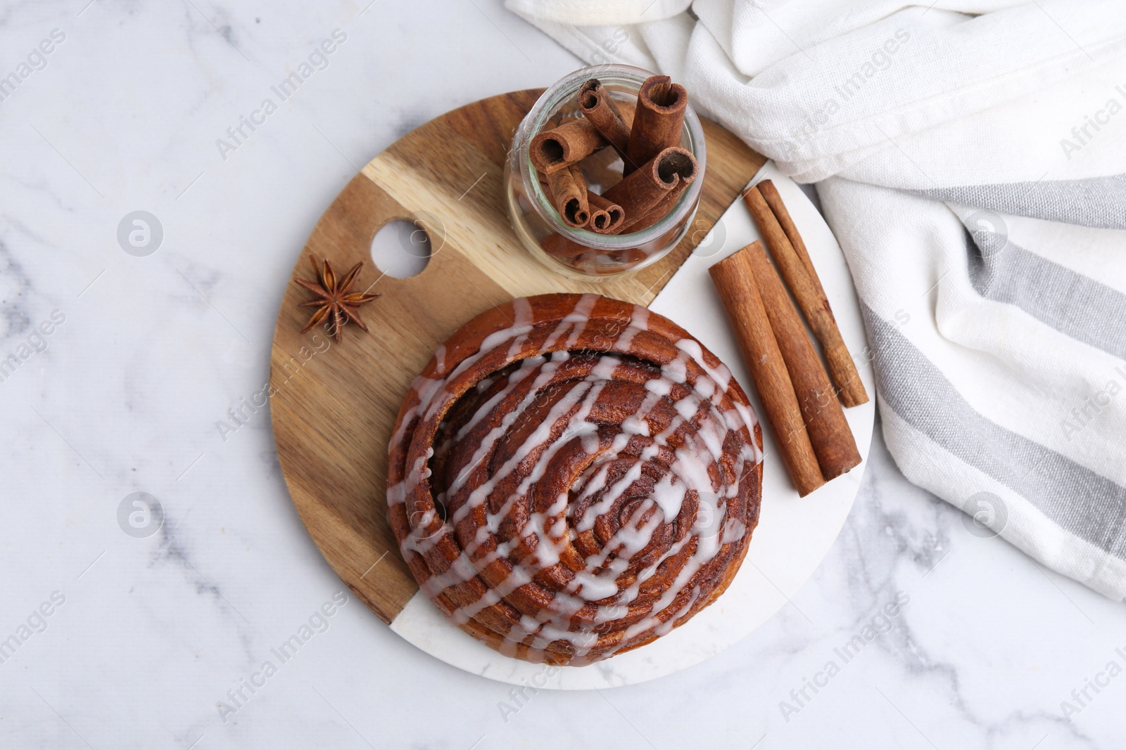 Photo of Tasty cinnamon roll with cream and spices on white marble table, top view