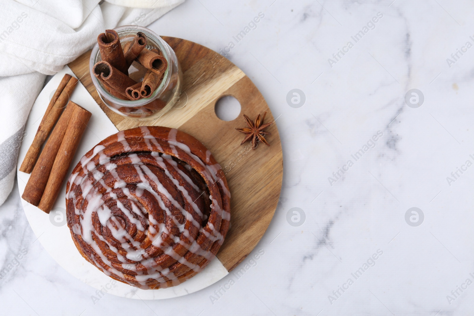 Photo of Tasty cinnamon roll with cream and spices on white marble table, top view. Space for text