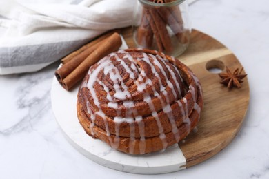 Photo of Tasty cinnamon roll with cream and spices on white marble table, closeup