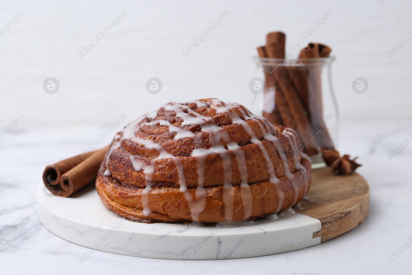 Photo of Tasty cinnamon roll with cream and spices on white table, closeup