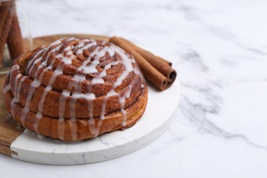 Photo of Tasty cinnamon roll with cream on white marble table, closeup. Space for text