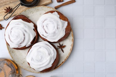 Photo of Tasty cinnamon rolls with cream, spices and tea on white tiled table, flat lay. Space for text