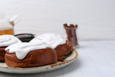 Photo of Tasty cinnamon rolls with cream and spices on white tiled table, closeup. Space for text