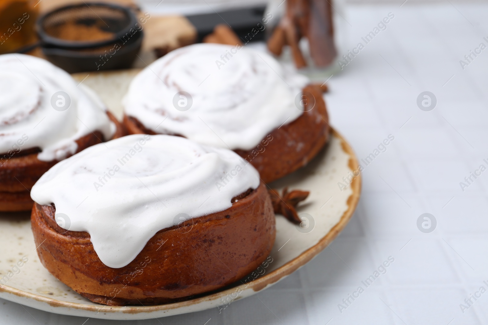 Photo of Tasty cinnamon rolls with cream and spices on white tiled table, closeup