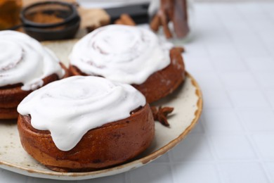 Photo of Tasty cinnamon rolls with cream and spices on white tiled table, closeup