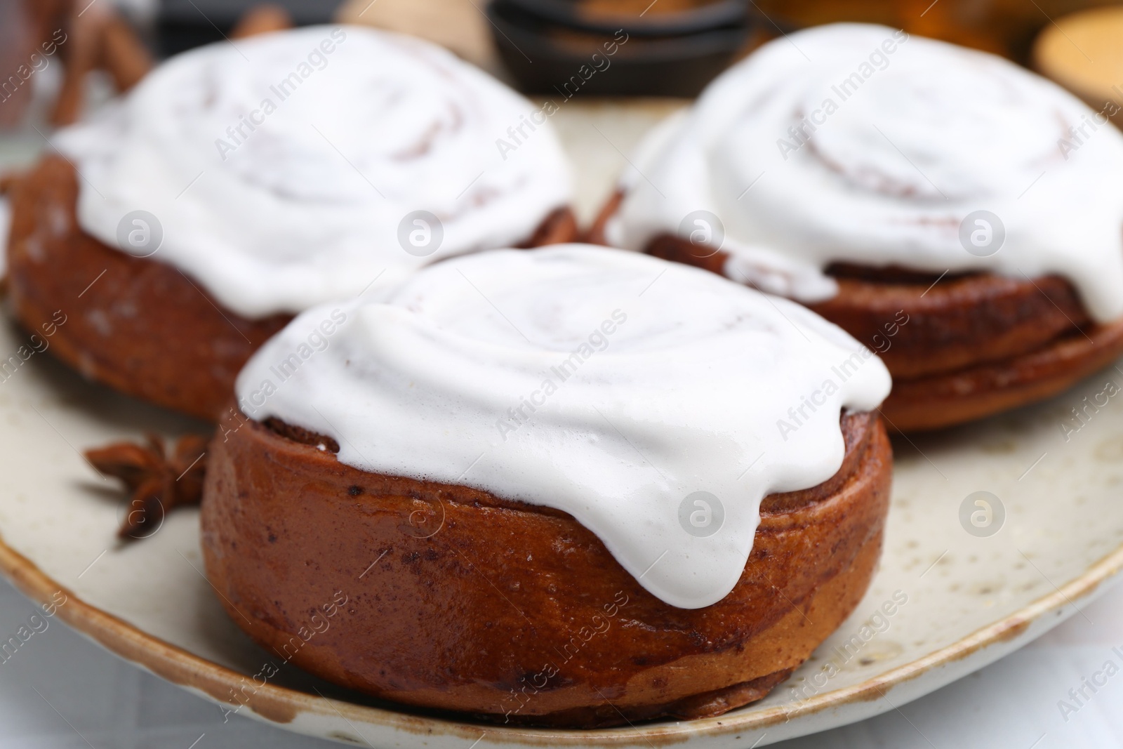 Photo of Tasty cinnamon rolls with cream and spices on white table, closeup