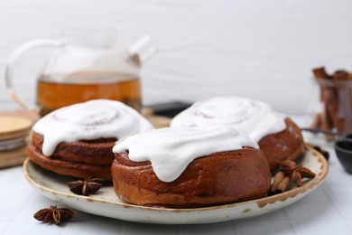 Photo of Tasty cinnamon rolls with cream and spices on white tiled table, closeup. Space for text