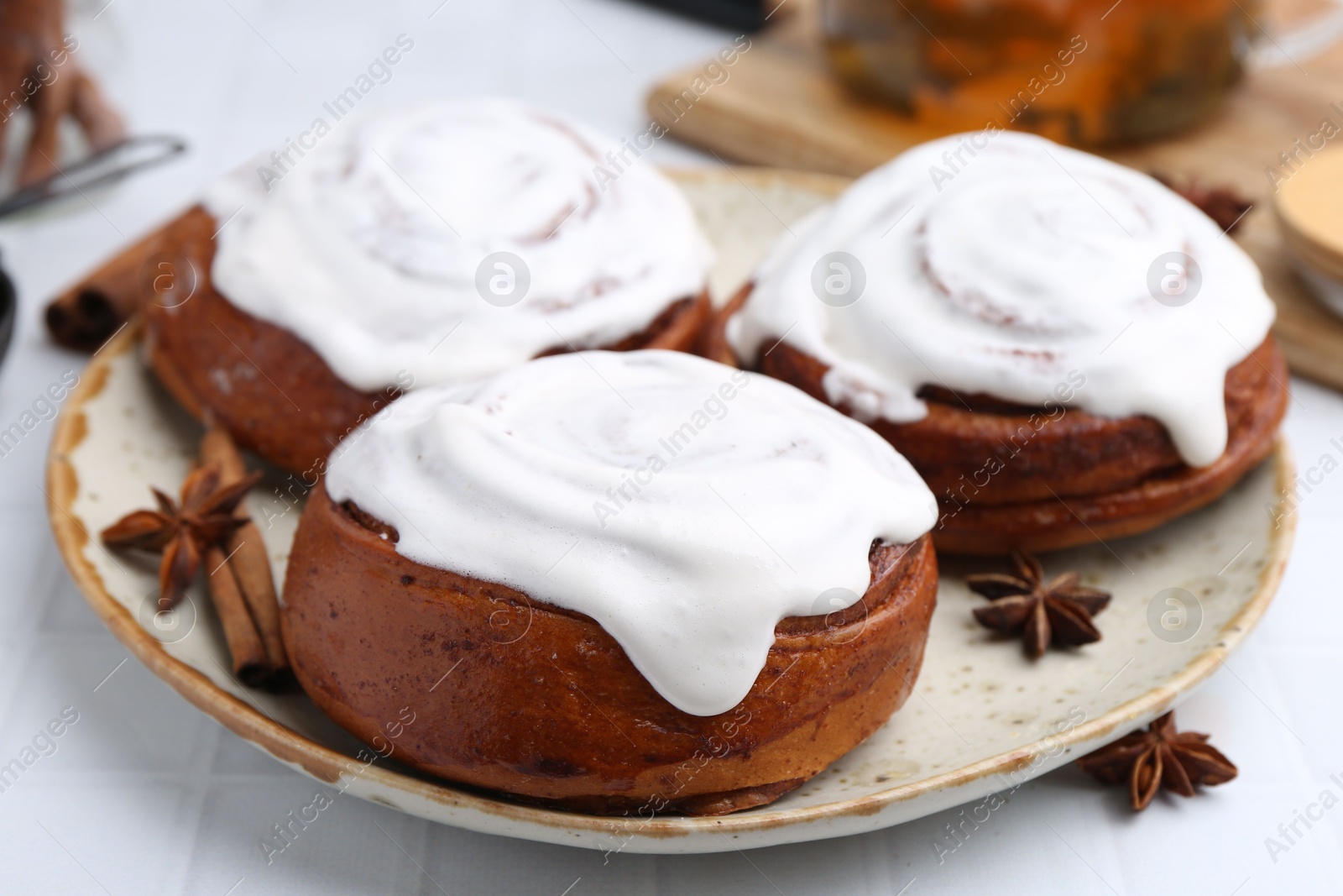 Photo of Tasty cinnamon rolls with cream and spices on white tiled table, closeup