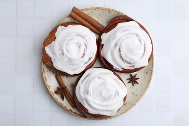 Photo of Tasty cinnamon rolls with cream and spices on white tiled table, top view