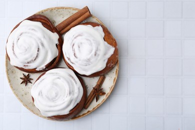 Photo of Tasty cinnamon rolls with cream and spices on white tiled table, top view. Space for text