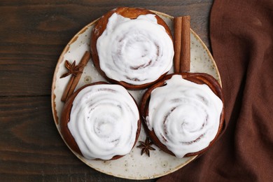 Photo of Tasty cinnamon rolls with cream and spices on wooden table, top view