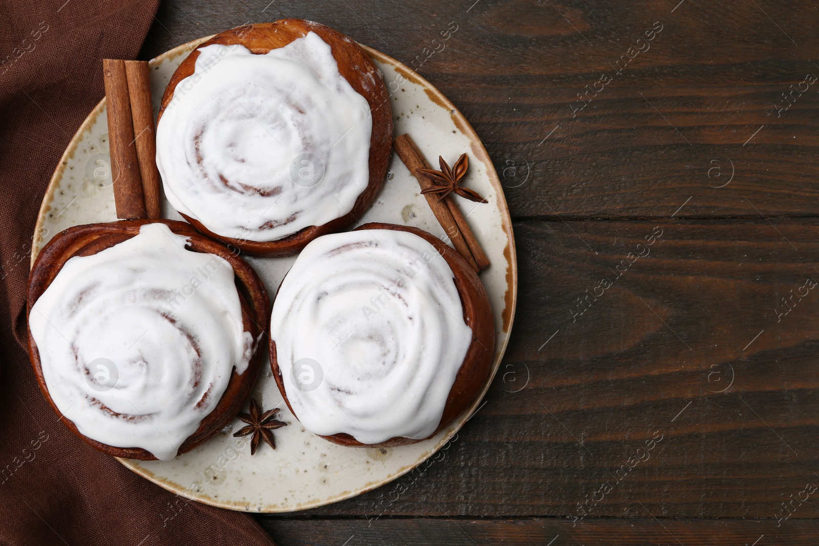 Photo of Tasty cinnamon rolls with cream and spices on wooden table, top view. Space for text