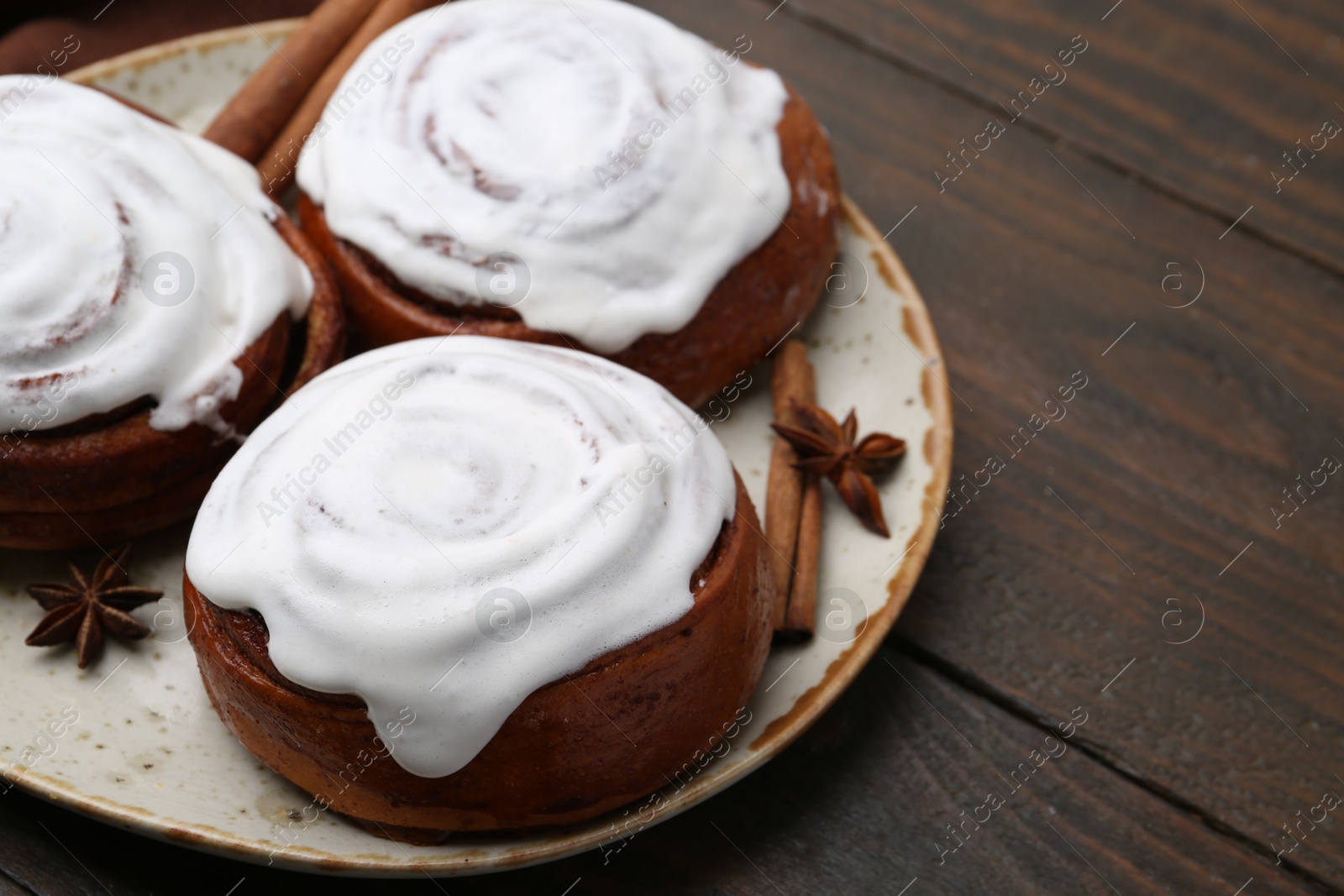 Photo of Tasty cinnamon rolls with cream and spices on wooden table, closeup