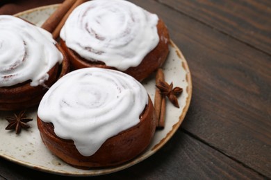 Photo of Tasty cinnamon rolls with cream and spices on wooden table, closeup