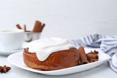 Photo of Tasty cinnamon roll with cream and spices on white table, closeup. Space for text