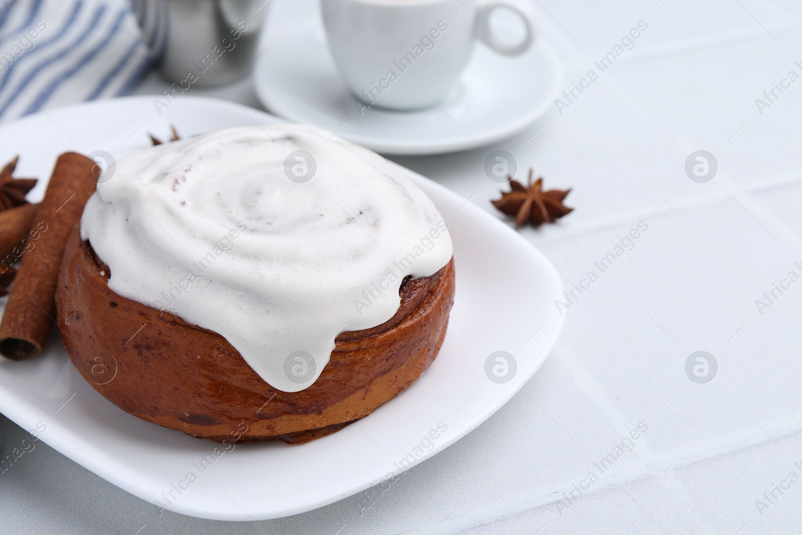 Photo of Tasty cinnamon roll with cream and spices on white tiled table, closeup