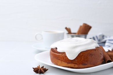 Photo of Tasty cinnamon roll with cream and spices on white table, closeup. Space for text