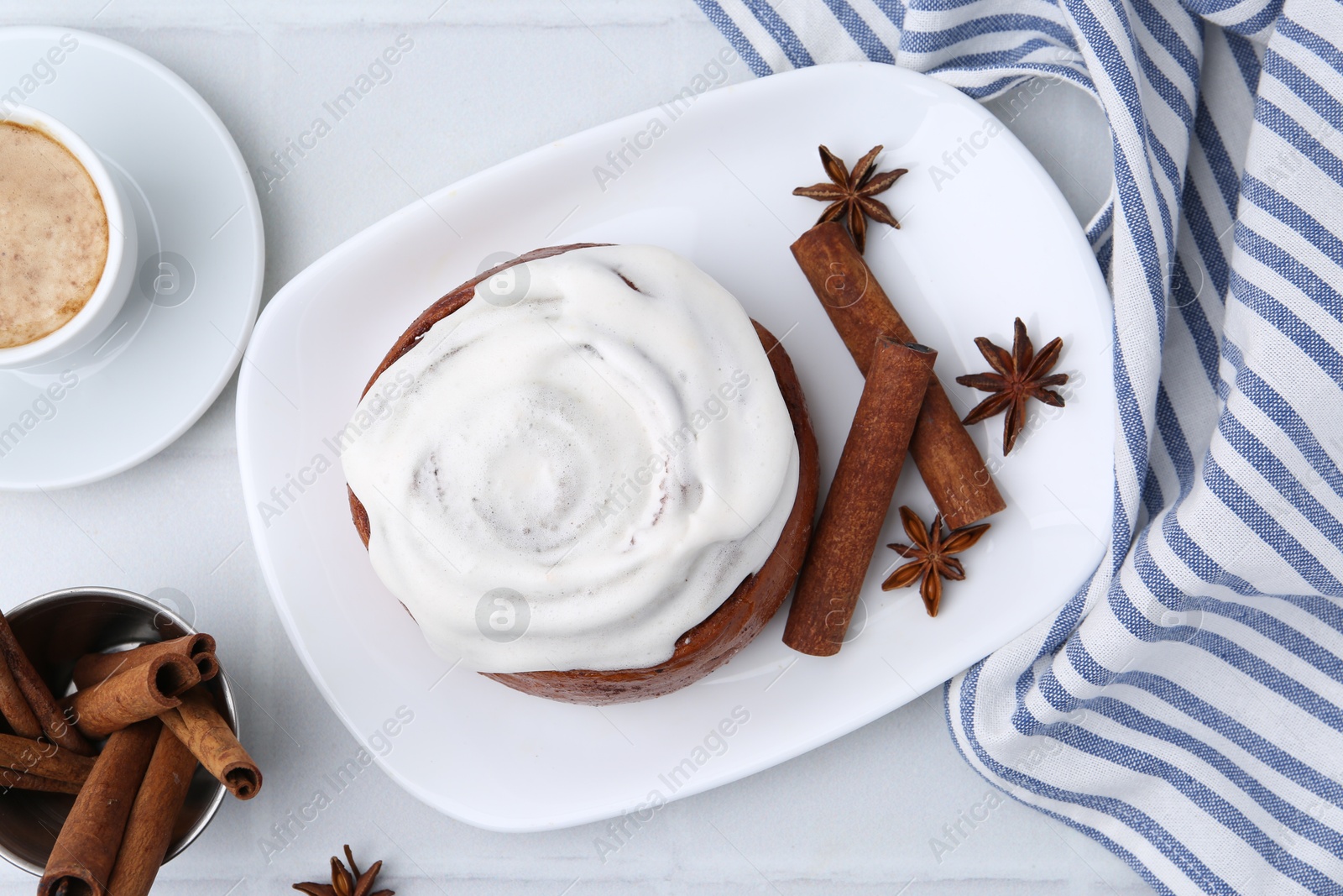 Photo of Tasty cinnamon roll with cream, spices and coffee on white tiled table, flat lay