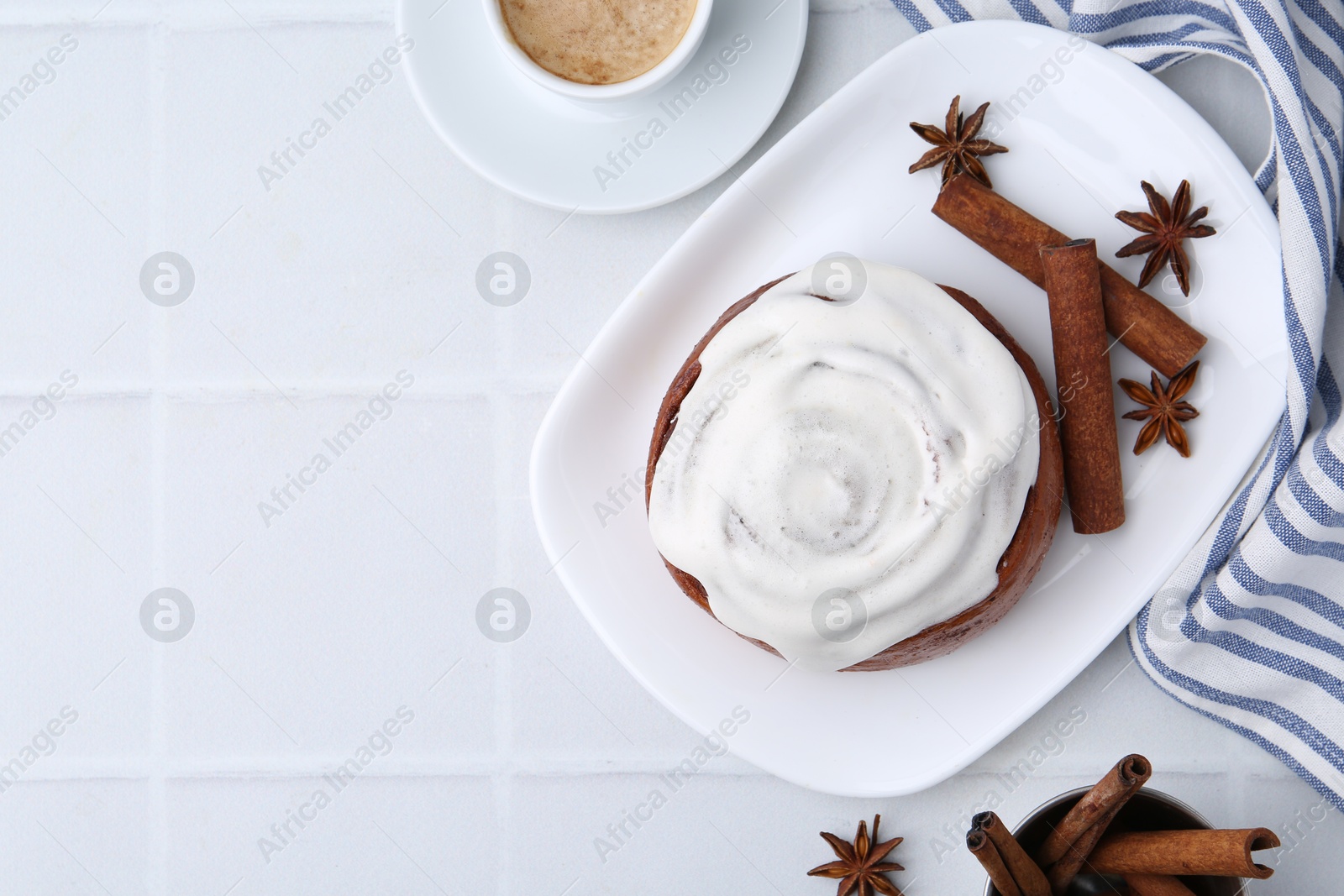 Photo of Tasty cinnamon roll with cream, spices and coffee on white tiled table, flat lay. Space for text