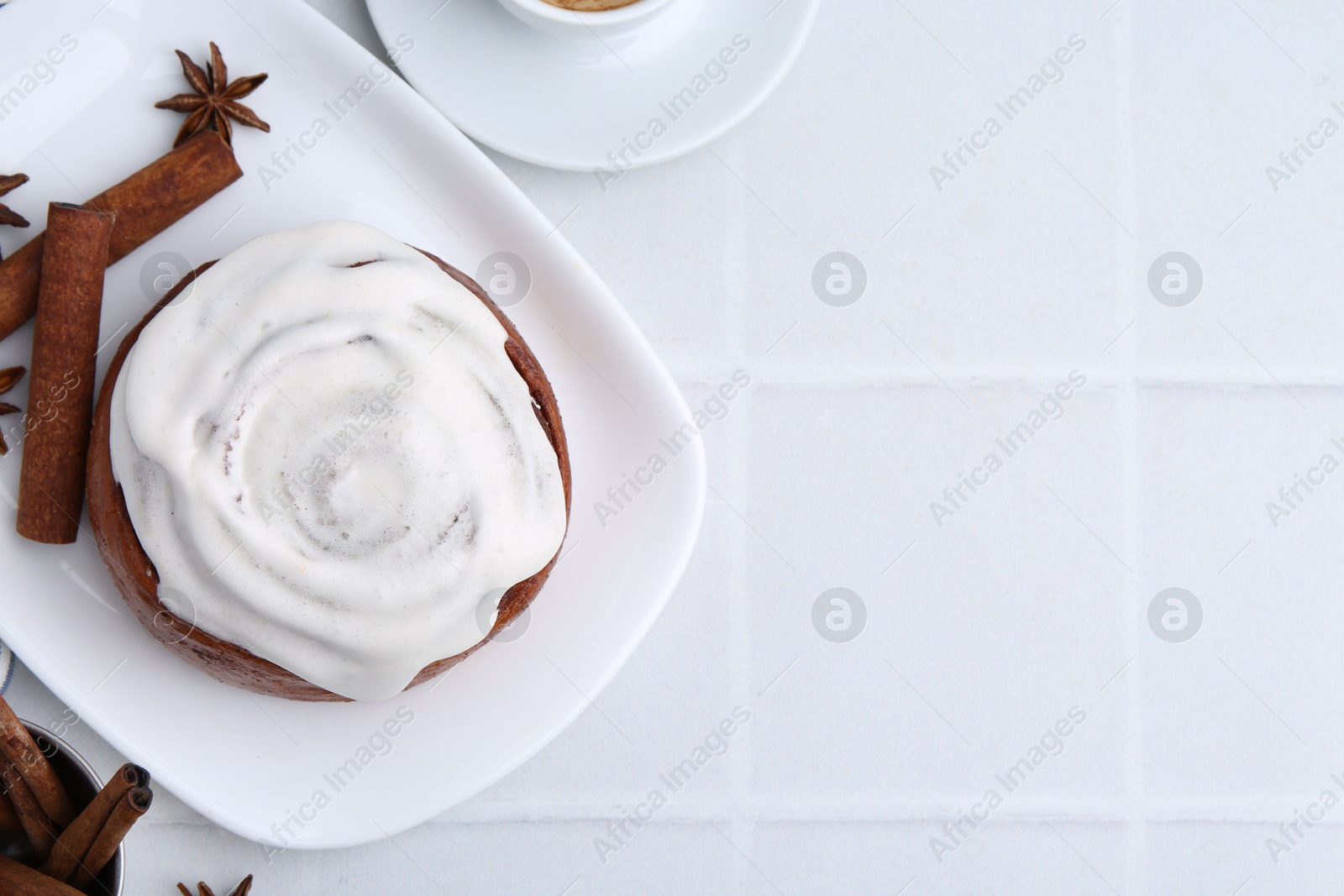 Photo of Tasty cinnamon roll with cream and spices on white tiled table, flat lay. Space for text