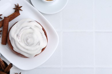 Photo of Tasty cinnamon roll with cream and spices on white tiled table, flat lay. Space for text