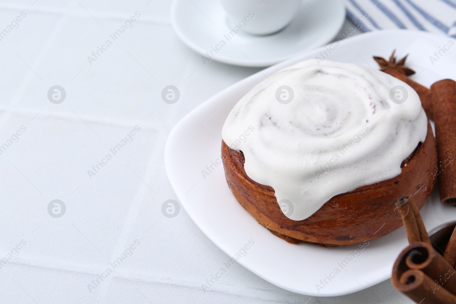 Photo of Tasty cinnamon roll with cream and spices on white tiled table, closeup. Space for text