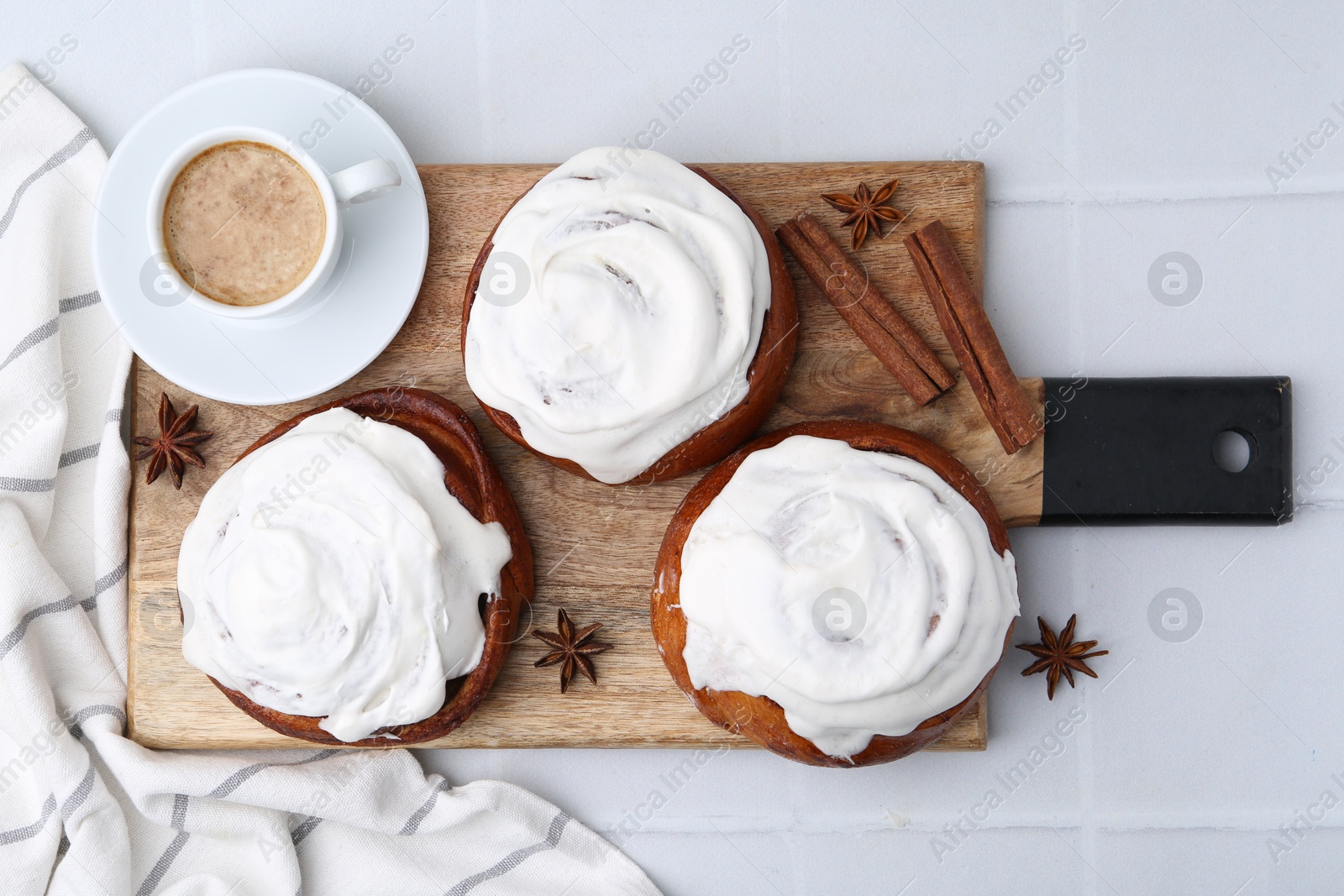 Photo of Tasty cinnamon rolls with cream, spices and coffee on white tiled table, flat lay