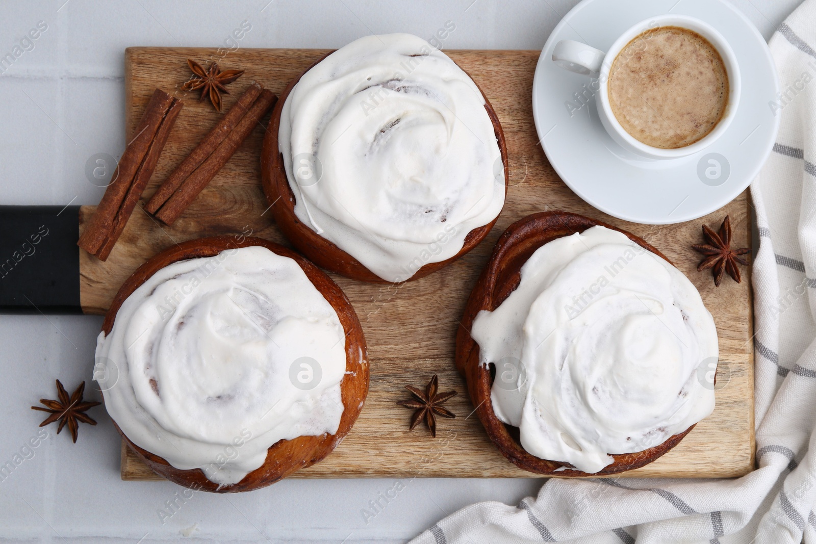 Photo of Tasty cinnamon rolls with cream, spices and coffee on white tiled table, flat lay