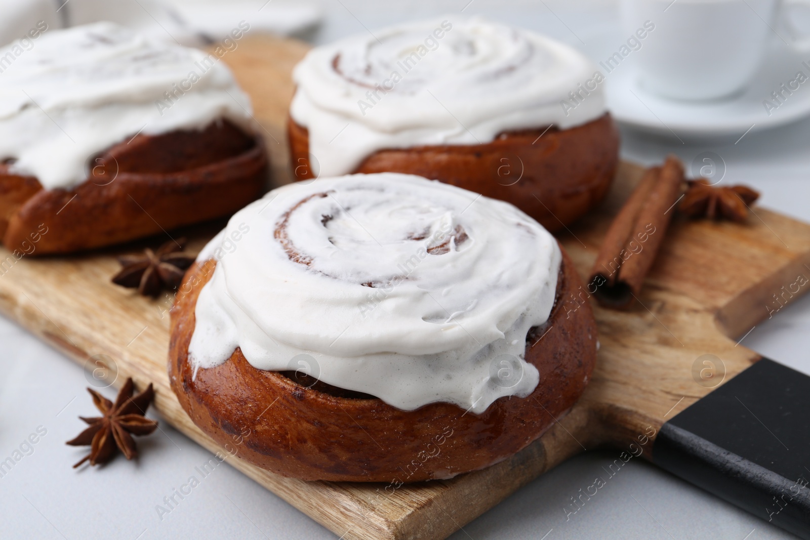 Photo of Tasty cinnamon rolls with cream and spices on white table, closeup