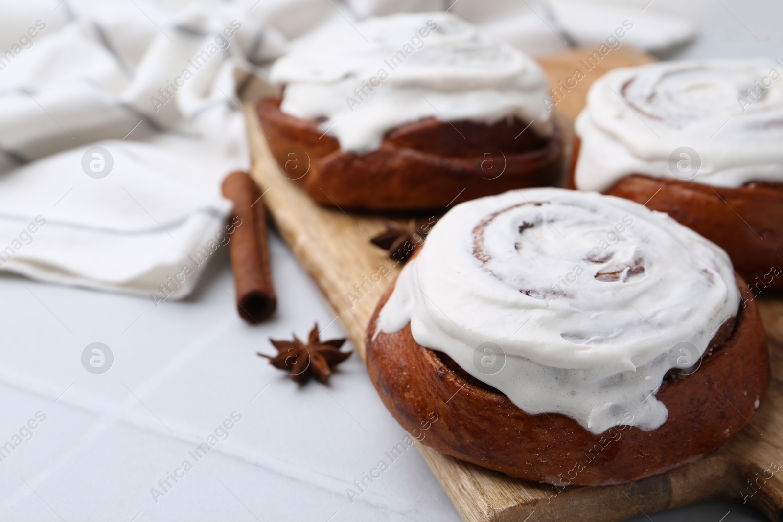 Photo of Tasty cinnamon rolls with cream and spices on white tiled table, closeup