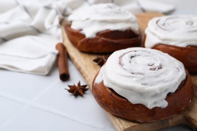 Photo of Tasty cinnamon rolls with cream and spices on white tiled table, closeup