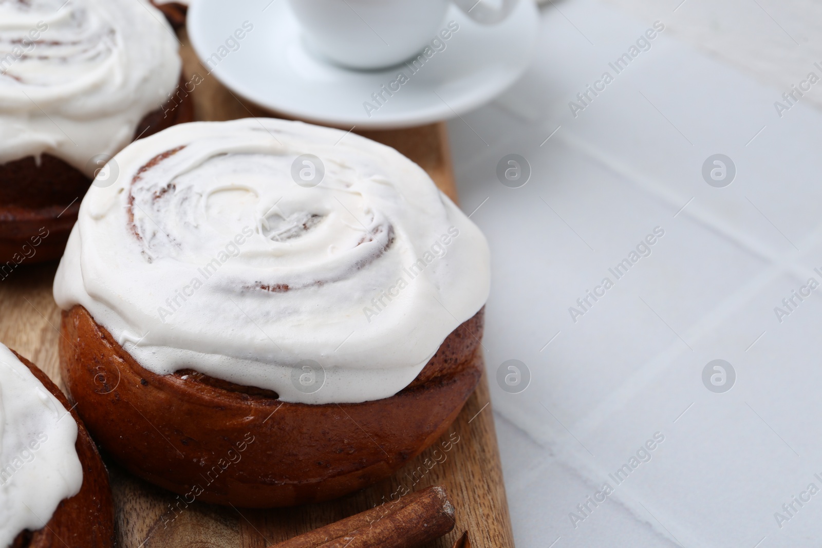 Photo of Tasty cinnamon rolls with cream on white tiled table, closeup