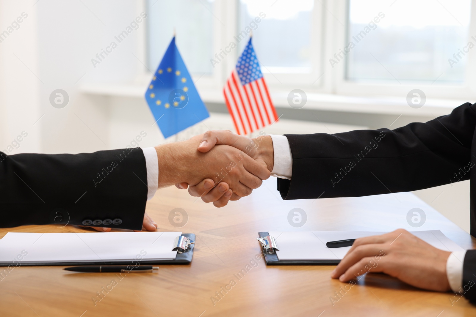 Photo of Diplomats shaking hands during meeting at wooden table indoors, closeup