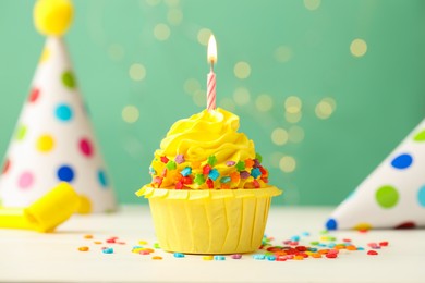 Photo of Tasty cupcake with burning candle and party cones on green background with blurred lights