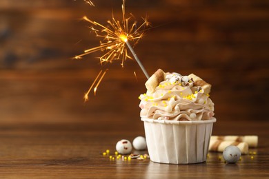 Photo of Tasty cupcake with burning sparkler on wooden table, space for text