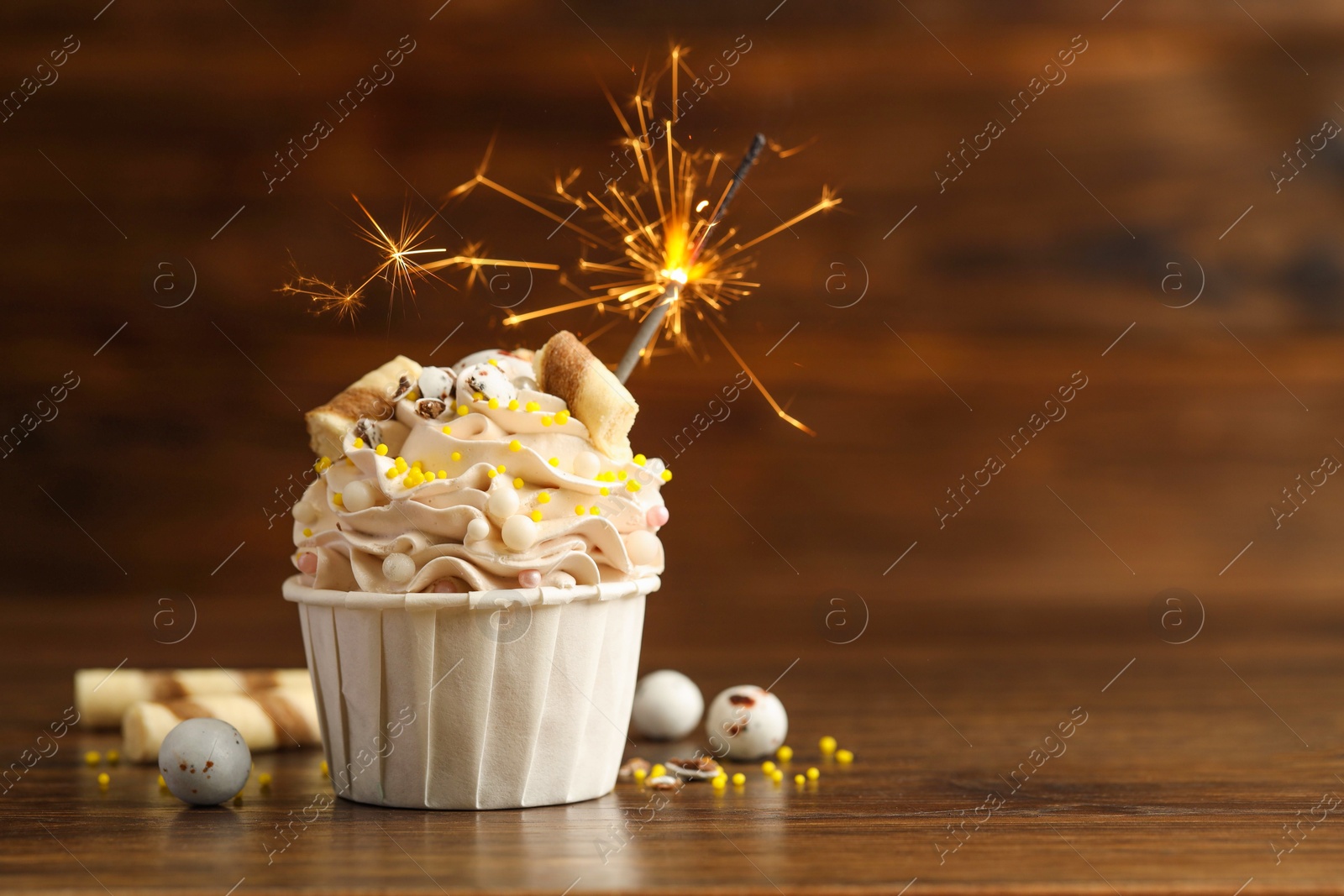 Photo of Tasty cupcake with burning sparkler on wooden table, space for text