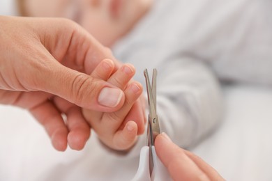 Photo of Mother cutting her cute little baby's nails on bed, closeup