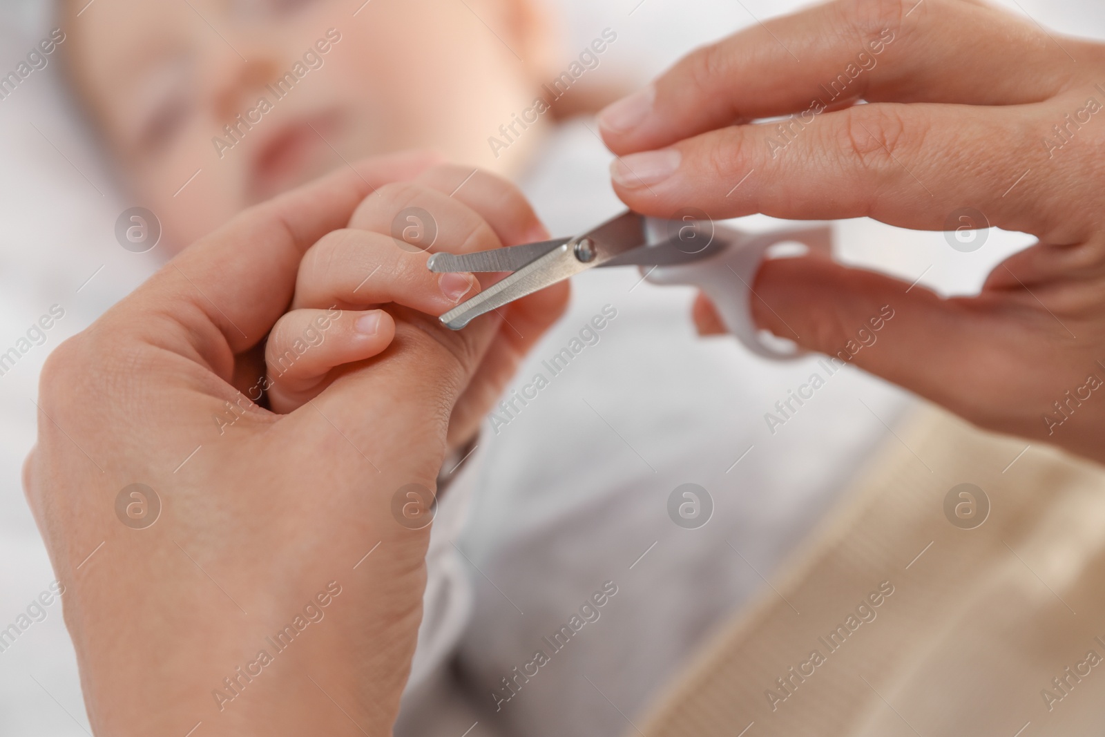 Photo of Mother cutting her cute little baby's nails on bed, closeup