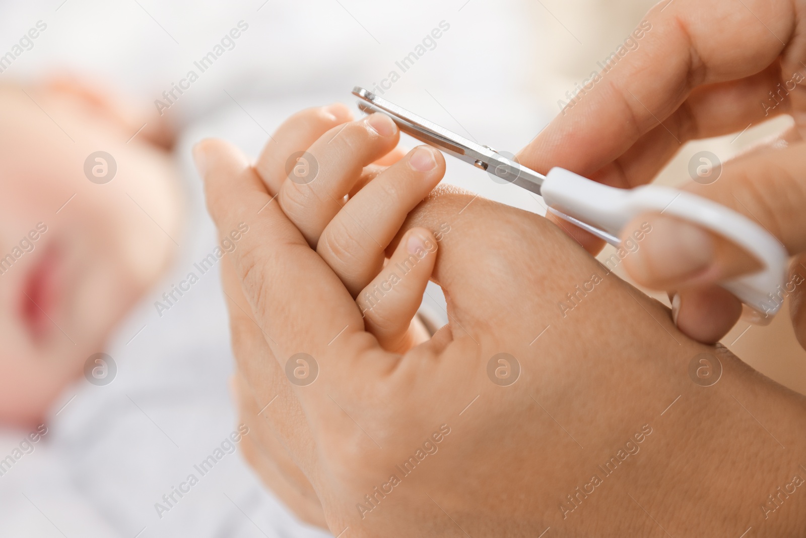 Photo of Mother cutting her cute little baby's nails on bed, closeup