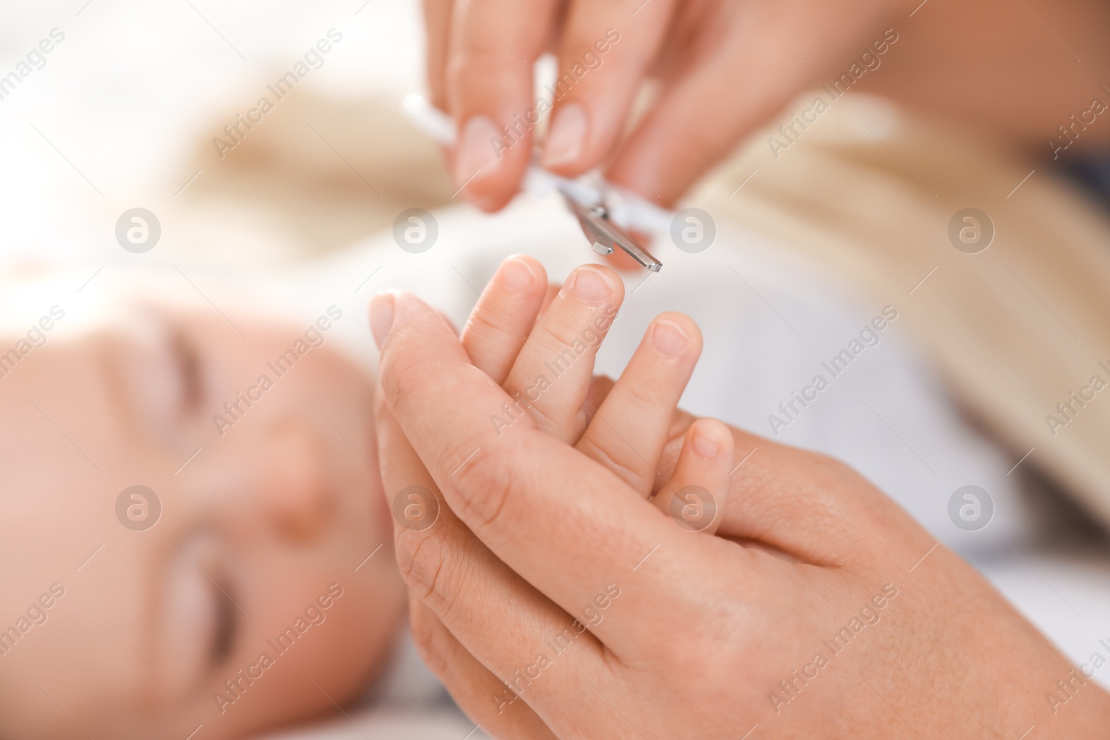 Photo of Mother cutting her cute little baby's nails on bed, closeup