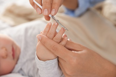 Photo of Mother cutting her cute little baby's nails on bed, closeup