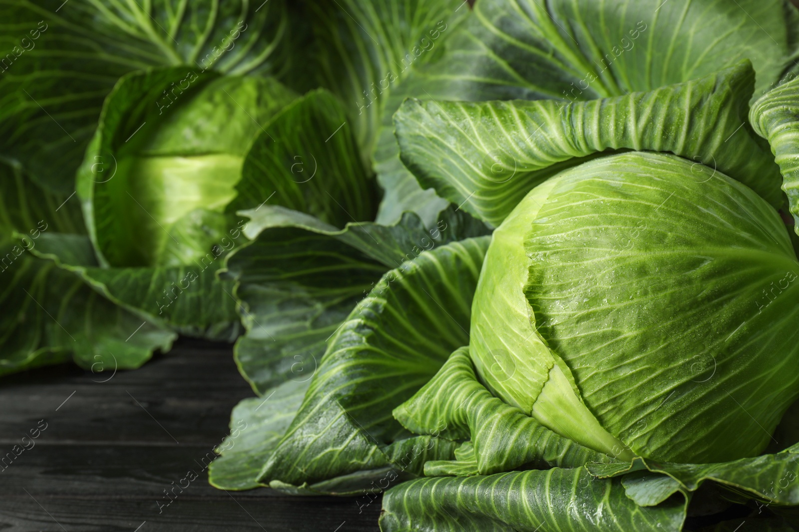 Photo of Ripe cabbages on black wooden table, closeup