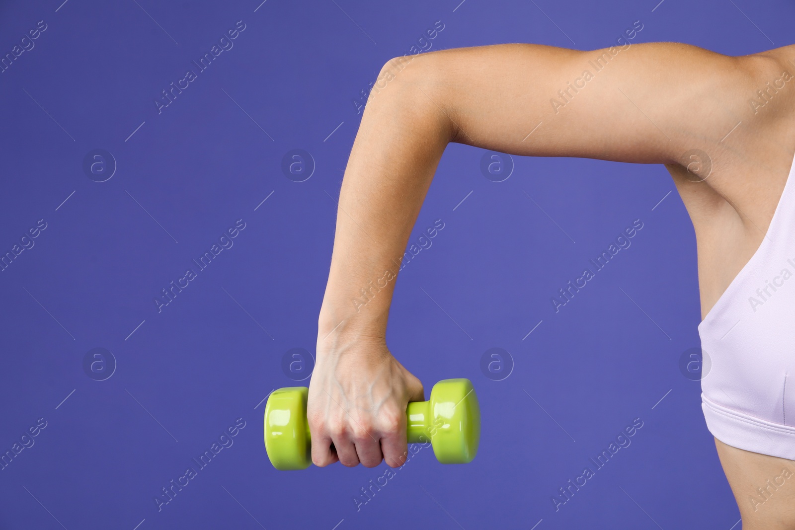 Photo of Woman exercising with dumbbell on purple background, closeup