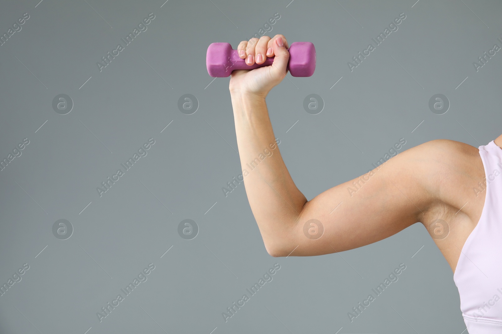 Photo of Woman exercising with dumbbell on light grey background, closeup. Space for text