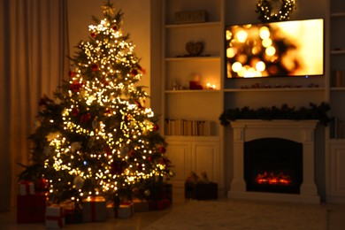 Photo of Blurred view of beautifully decorated Christmas tree near fireplace in room. Festive interior design