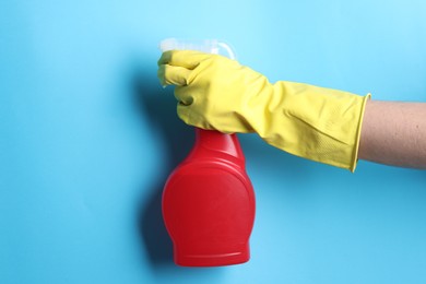 Photo of Woman with spray bottle of cleaning product on light blue background, closeup