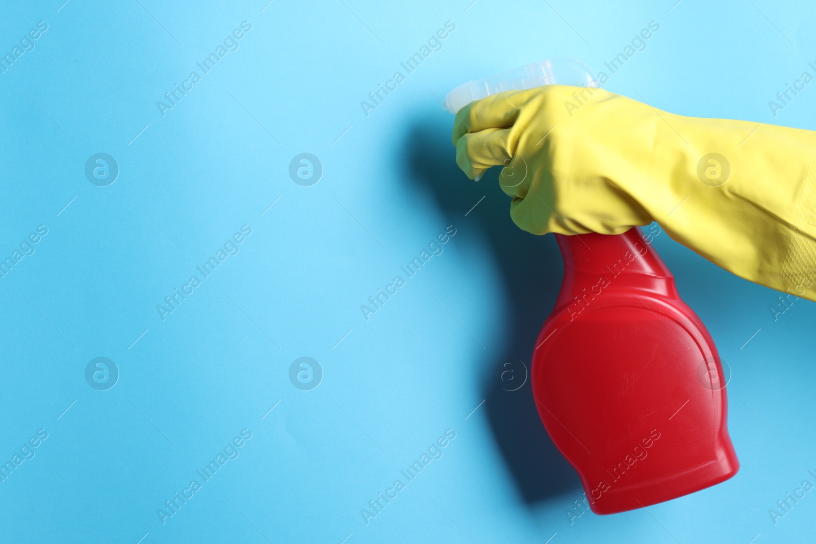 Photo of Woman with spray bottle of cleaning product on light blue background, closeup. Space for text