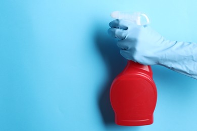 Photo of Woman with spray bottle of cleaning product on light blue background, closeup. Space for text