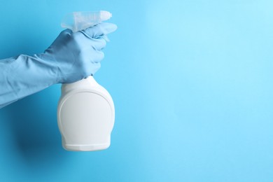 Photo of Woman with spray bottle of cleaning product on light blue background, closeup. Space for text